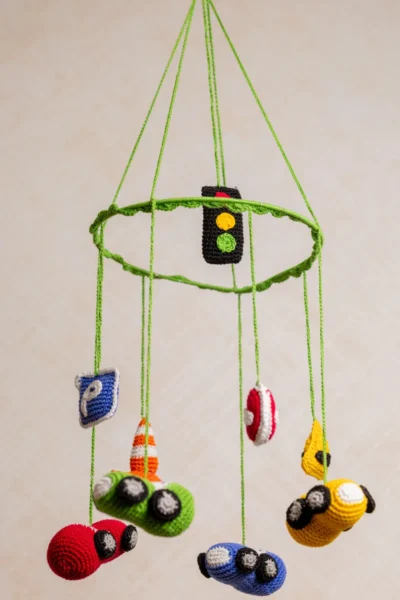 Close up of handmade crochet car nursery mobile showing individual miniature car detail and bright yarn stitch work