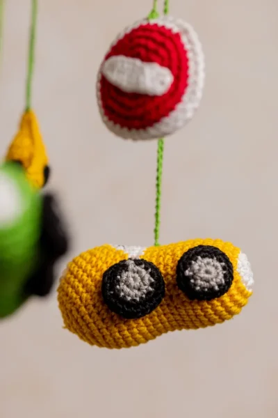 Close up of handmade crochet car nursery mobile showing individual miniature car detail and bright yarn stitch work