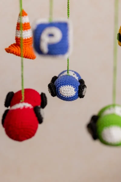Close up of handmade crochet car nursery mobile showing individual miniature car detail and bright yarn stitch work
