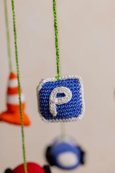 Close up of handmade crochet car nursery mobile showing individual miniature car detail and bright yarn stitch work