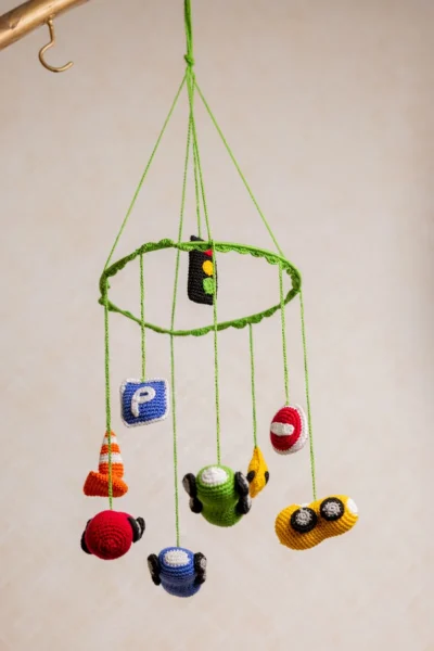 Close up of handmade crochet car nursery mobile showing individual miniature car detail and bright yarn stitch work
