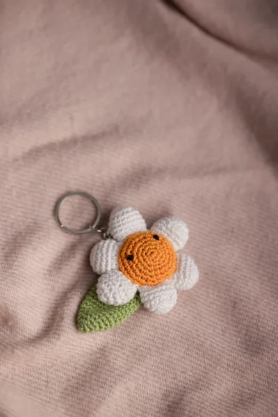 Close up of handmade white daisy crochet keyring showing petal stitch detail and sunny yellow centre