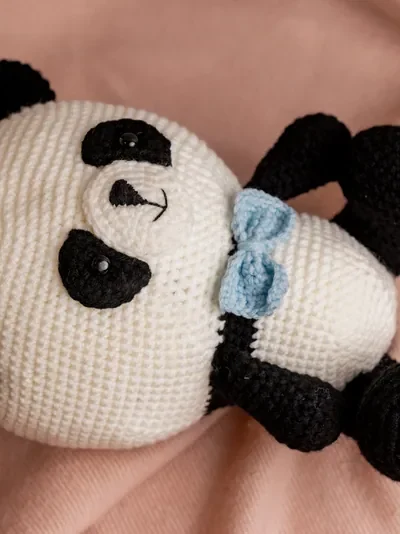 Full body view of crochet panda bear with blue bow showing soft black and white yarn construction and friendly expression Melbourne