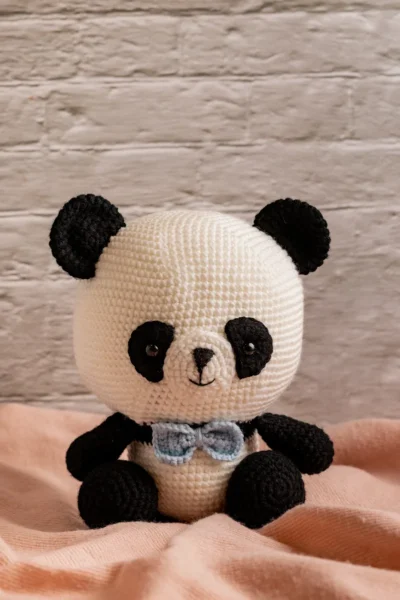 Full body view of crochet panda bear with blue bow showing soft black and white yarn construction and friendly expression Melbourne