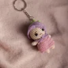 Close up of handmade mini crochet doll keyring showing pink yarn hair and purple dress stitch detail