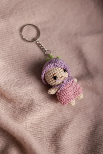 Close up of handmade mini crochet doll keyring showing pink yarn hair and purple dress stitch detail
