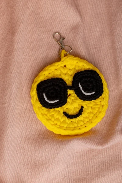Close up of handmade smiley face bag charm showing crochet stitch detail and cheerful yellow yarn