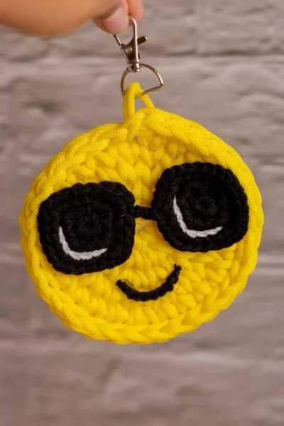 Close up of handmade smiley face bag charm showing crochet stitch detail and cheerful yellow yarn