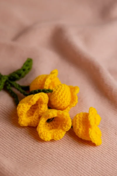 Close up of handmade yellow tulip flower bag charm showing crochet stitch detail and green stem