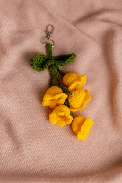 Close up of handmade yellow tulip flower bag charm showing crochet stitch detail and green stem