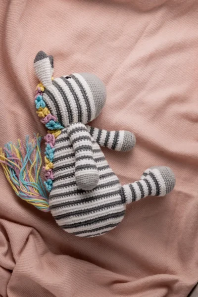 Full body view of crochet Zippy zebra showing black and white stripe pattern and bright multicolour rainbow mane Melbourne