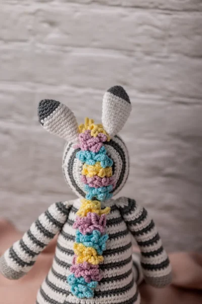 Full body view of crochet Zippy zebra showing black and white stripe pattern and bright multicolour rainbow mane Melbourne